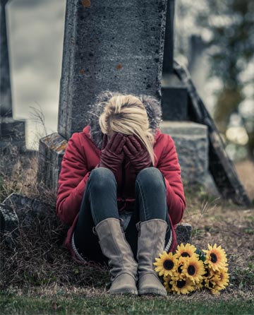 Grieving woman sitting by a gravesite with sunflowers, reflecting the need for a support group for grieving parents.